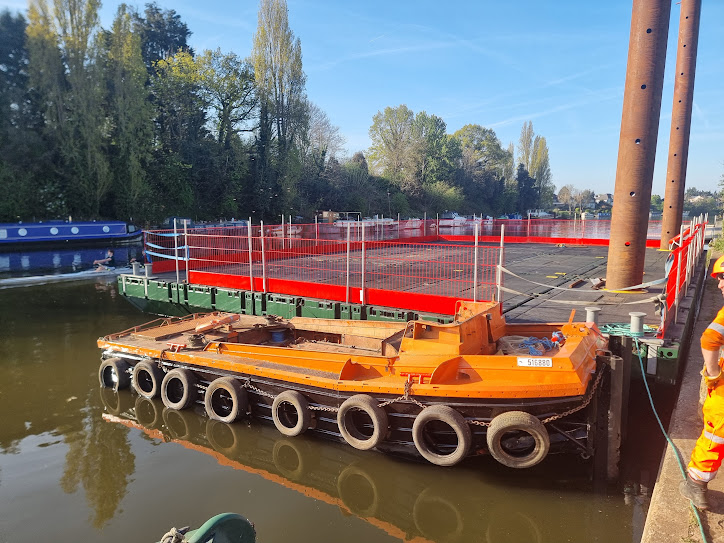 Orange tug alongside a pontoon working platform on a waterway