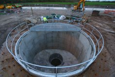 Circular concrete-lined shaft with a steel cover and handrails on an open site