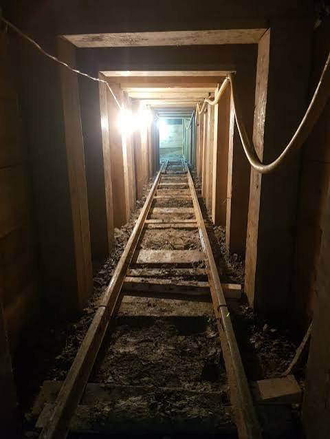 Timber-supported heading lit by work lights, with a narrow rail track running through it