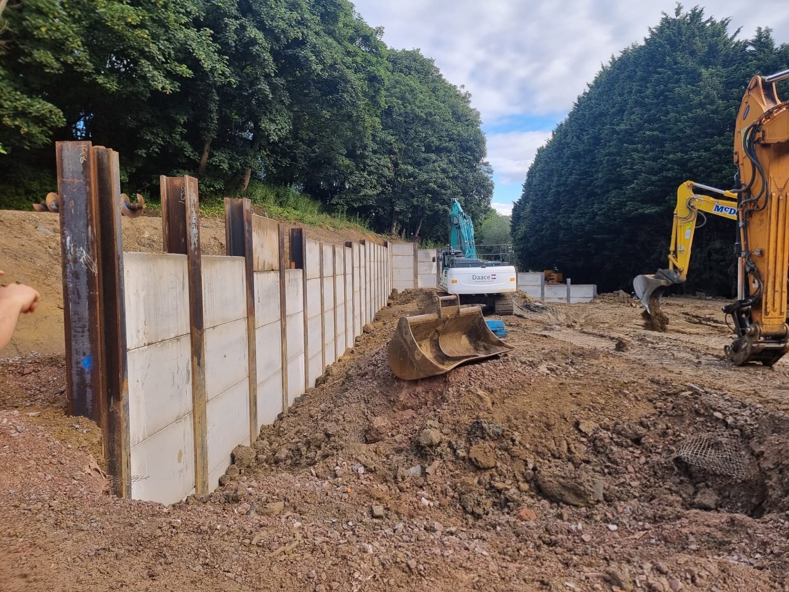Concrete panels being installed between steel king posts to form a retaining wall on a sloping site