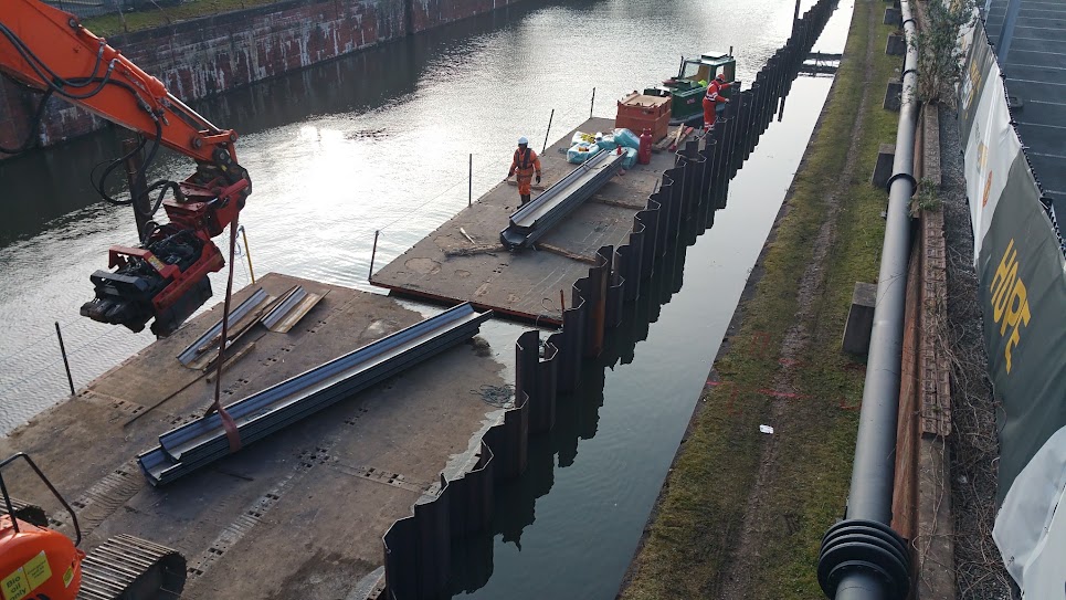 Sheet piles being installed beside a canal from a floating working platform