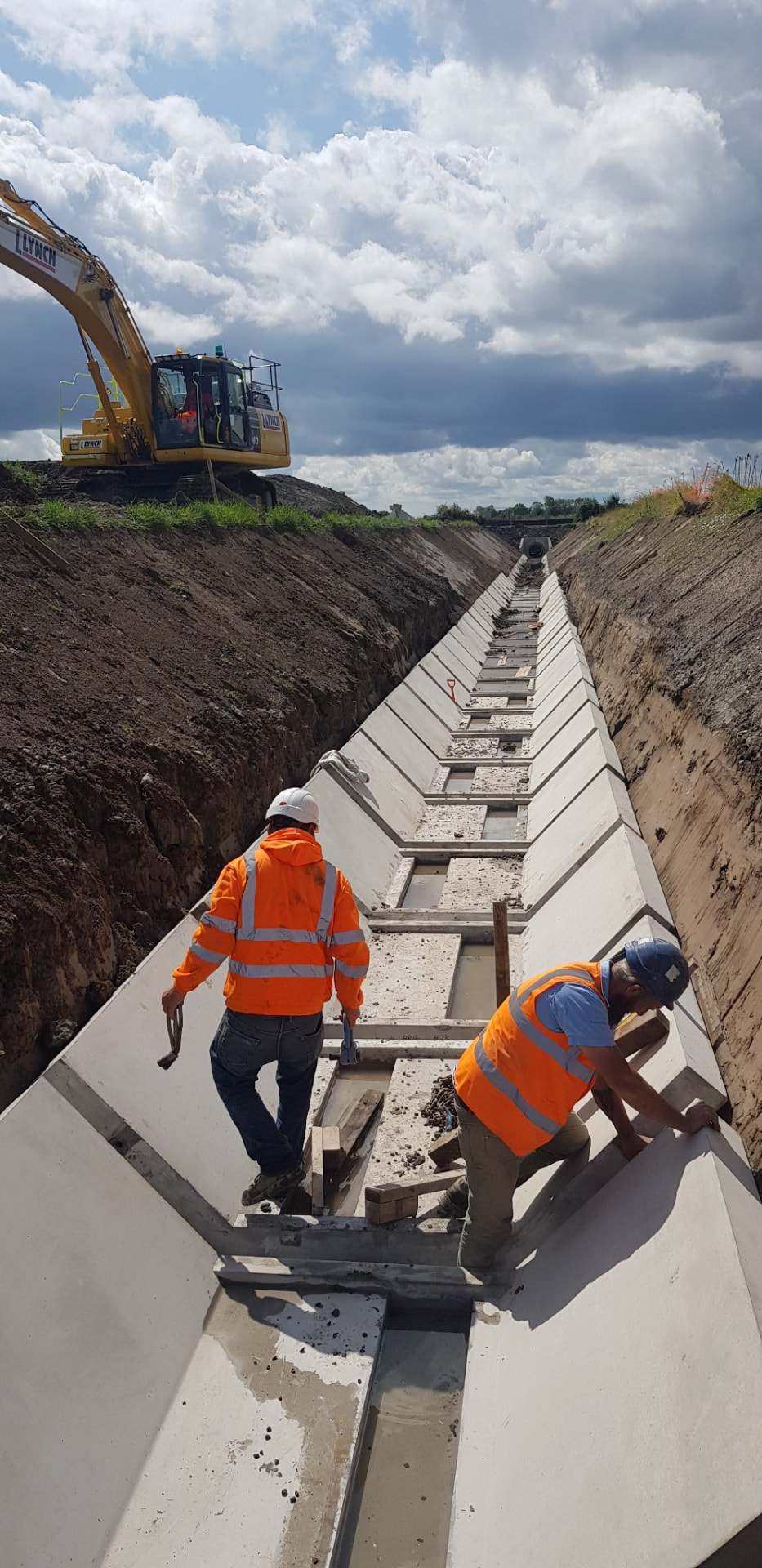 Two workers installing precast concrete units in a long lined excavation